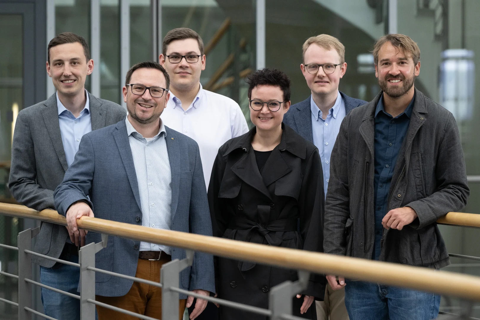 Eine Wissenschaftlerin und ein Wissenschaftler arbeiten hinter einer Glasfassade und mischen Chemikalien mit Großgeräten.