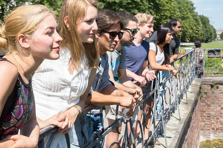 Eine Wissenschaftlerin und ein Wissenschaftler arbeiten hinter einer Glasfassade und mischen Chemikalien mit Großgeräten.